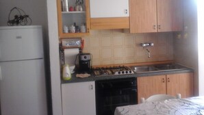 Cocina compacta con refrigerador, estufa, lavamanos y gabinetes de madera.