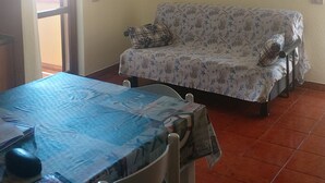 Un comedor con una mesa cubierta con mantel azul, un ventilador de techo y un sofá estampado con motivos florales.