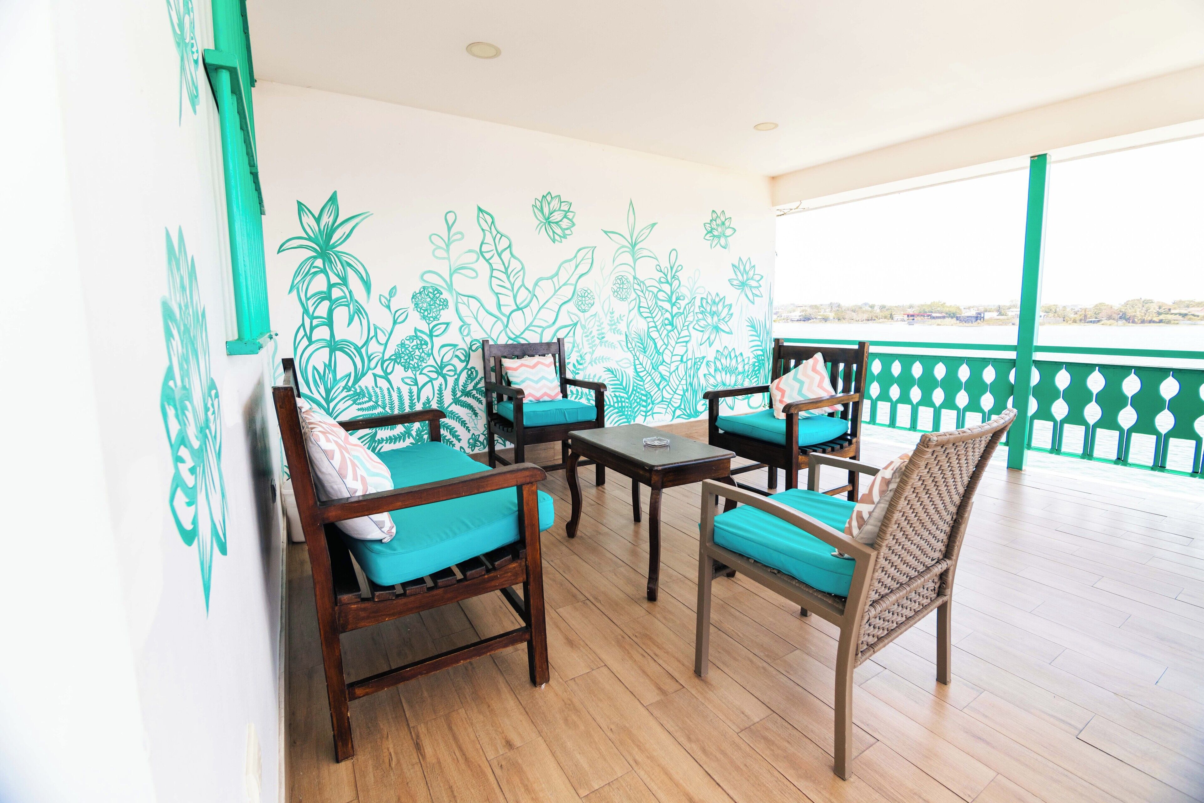A balcony with wooden flooring, four wooden chairs with teal cushions, and a table.