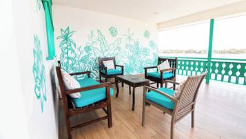 A balcony with wooden flooring, four wooden chairs with teal cushions, and a table.