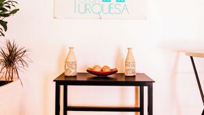 A room with a wooden floor, a black table with two decorative vases, a bowl with oranges, and a sign on the wall reading "CASA TURQUESA". - Hotel Casa Turquesa (Flores)