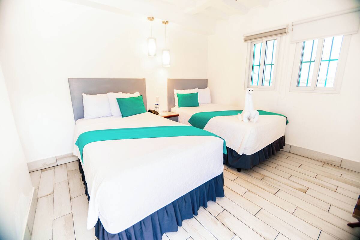 A hotel room with two beds, each with a white and teal bedspread, and a wooden floor.
