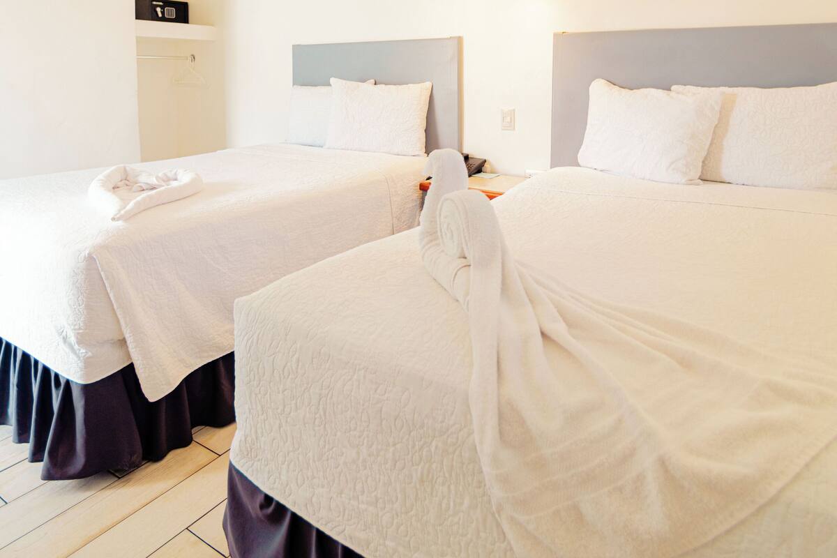 A hotel room with two beds, a ceiling fan, and wall-mounted light fixtures.