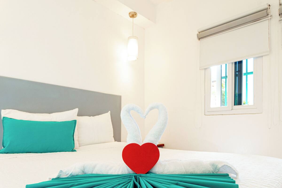 A neatly made bed with a heart-shaped towel arrangement and a red heart decoration.