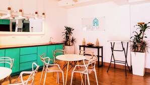 A modern interior with a wooden floor, white chairs, a round table, a green counter, and a ceiling fan. - Hotel Casa Turquesa (Flores)