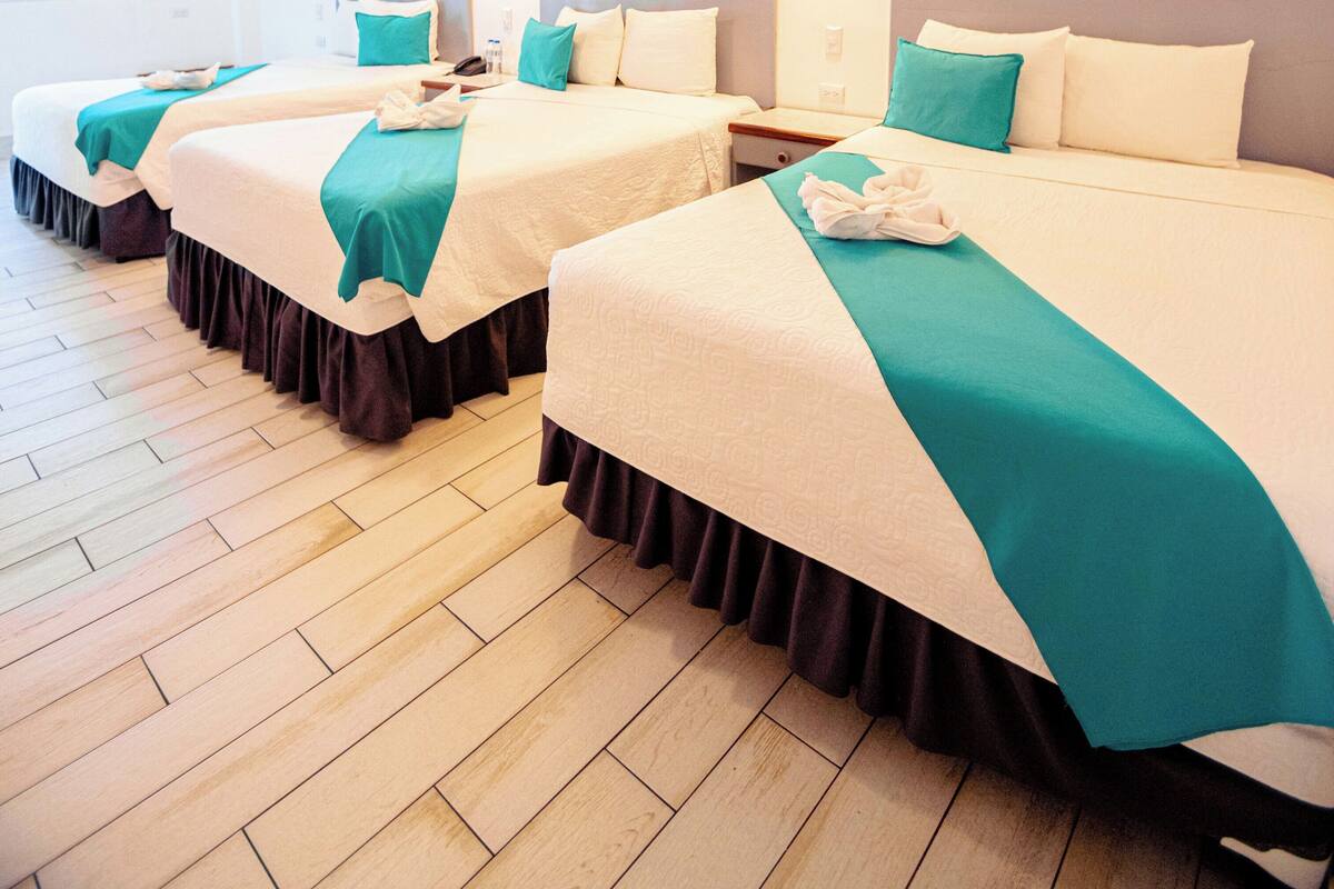A hotel room with four beds arranged in a row, each with a teal bedspread and white bedding.