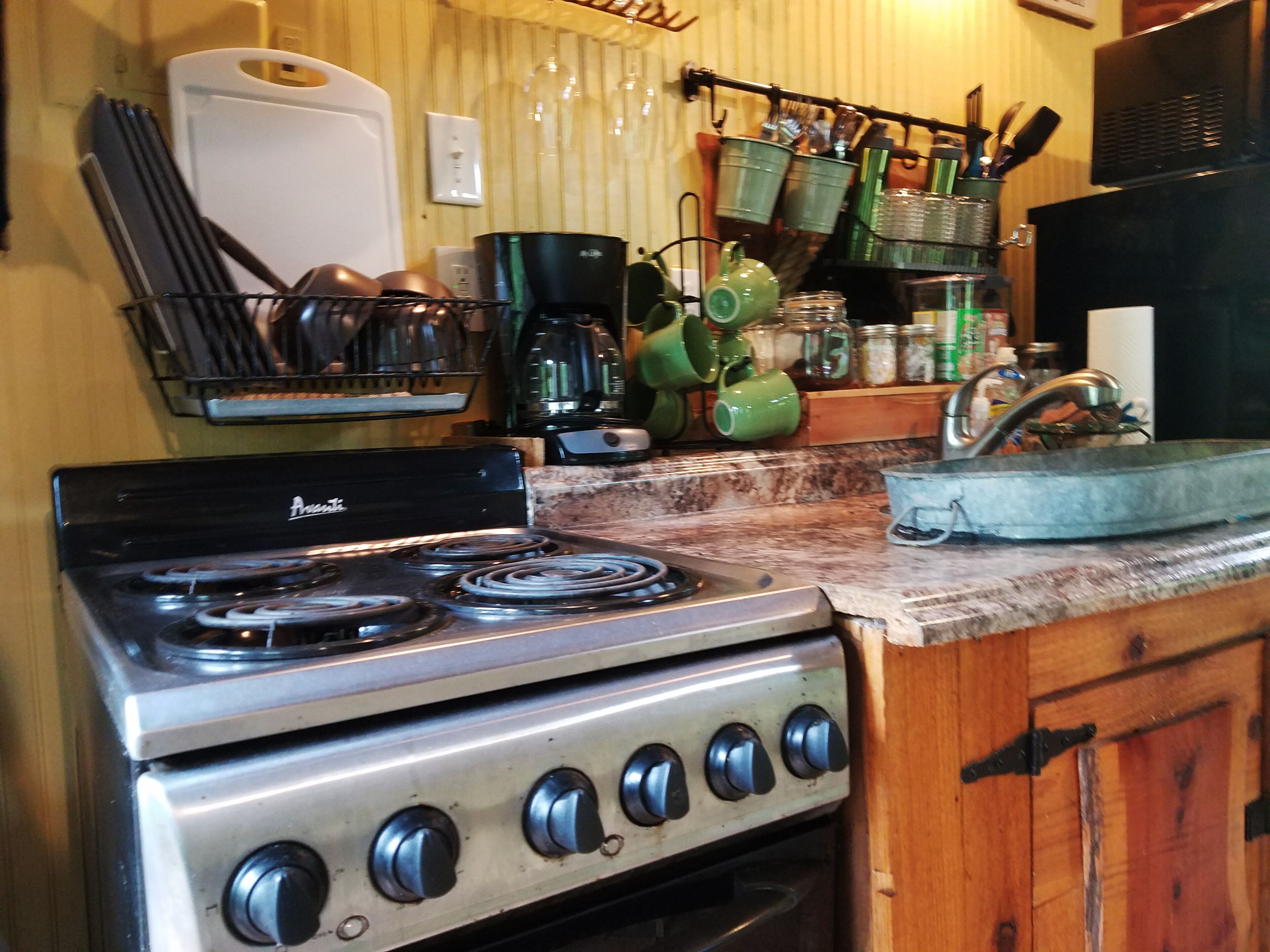 Una cocina con estufa, cafetera y diferentes utensilios.