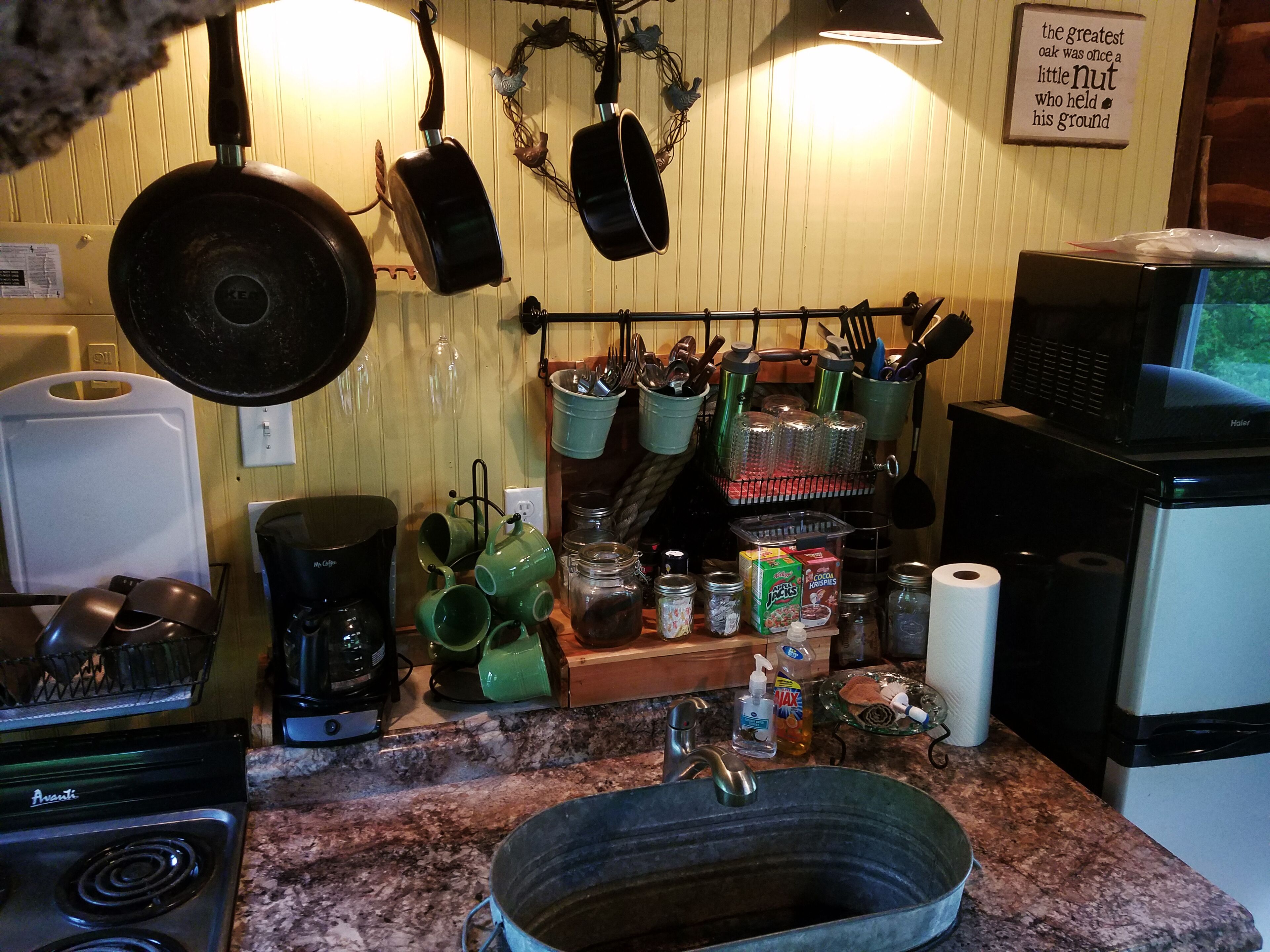 Una cocina con estufa, microondas y diferentes utensilios y electrodomésticos.