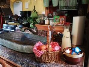 A kitchen counter with a large metal sink, a wicker basket with eggs, a bowl of yogurt, and various kitchen items.