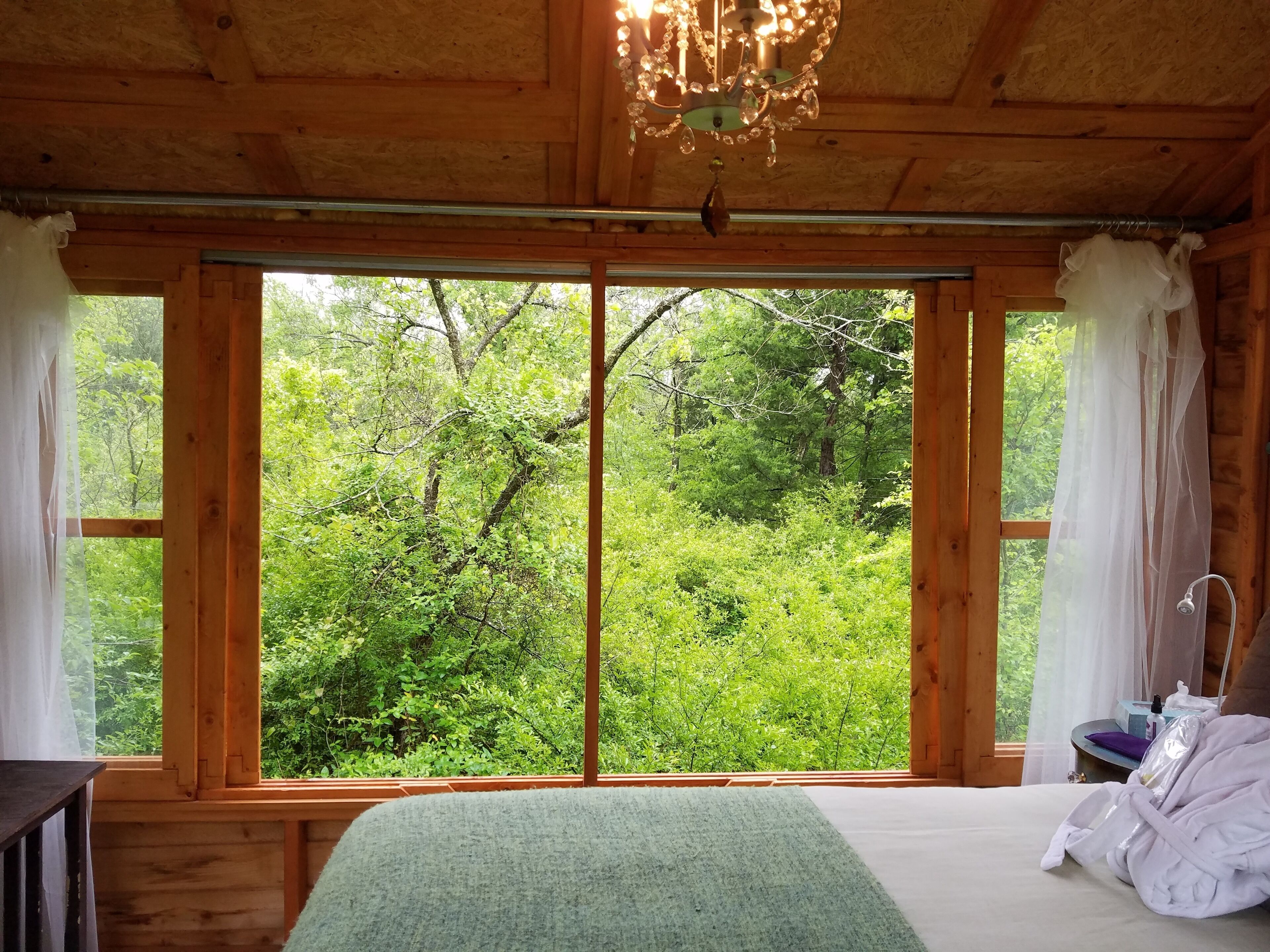 Ein Holzhütten-Zimmer mit großem Fenster, einem Bett und einer Chandelüster.