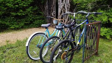 A bicycle rack with two bicycles parked, surrounded by greenery and a wooden structure.