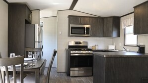 A modern kitchen with dark wood cabinets, stainless steel appliances, and a dining area with chairs and a table set for two. - Great Blue Resorts - Cherry Beach Resort (Prince Edward)