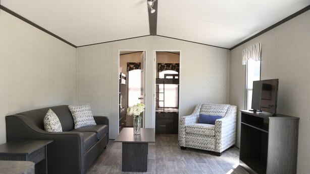 A modern living room with a sofa, armchair, coffee table, and a TV stand. - Great Blue Resorts - Cherry Beach Resort (Prince Edward)