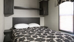 A bedroom with a bed, two nightstands, a headboard, and a window with blinds. - Great Blue Resorts - Cherry Beach Resort (Prince Edward)