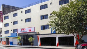 Un edificio de hotel con múltiples ventanas, un letrero que dice 'OYO HOTEL BRAZIL' y un árbol en la parte delantera.