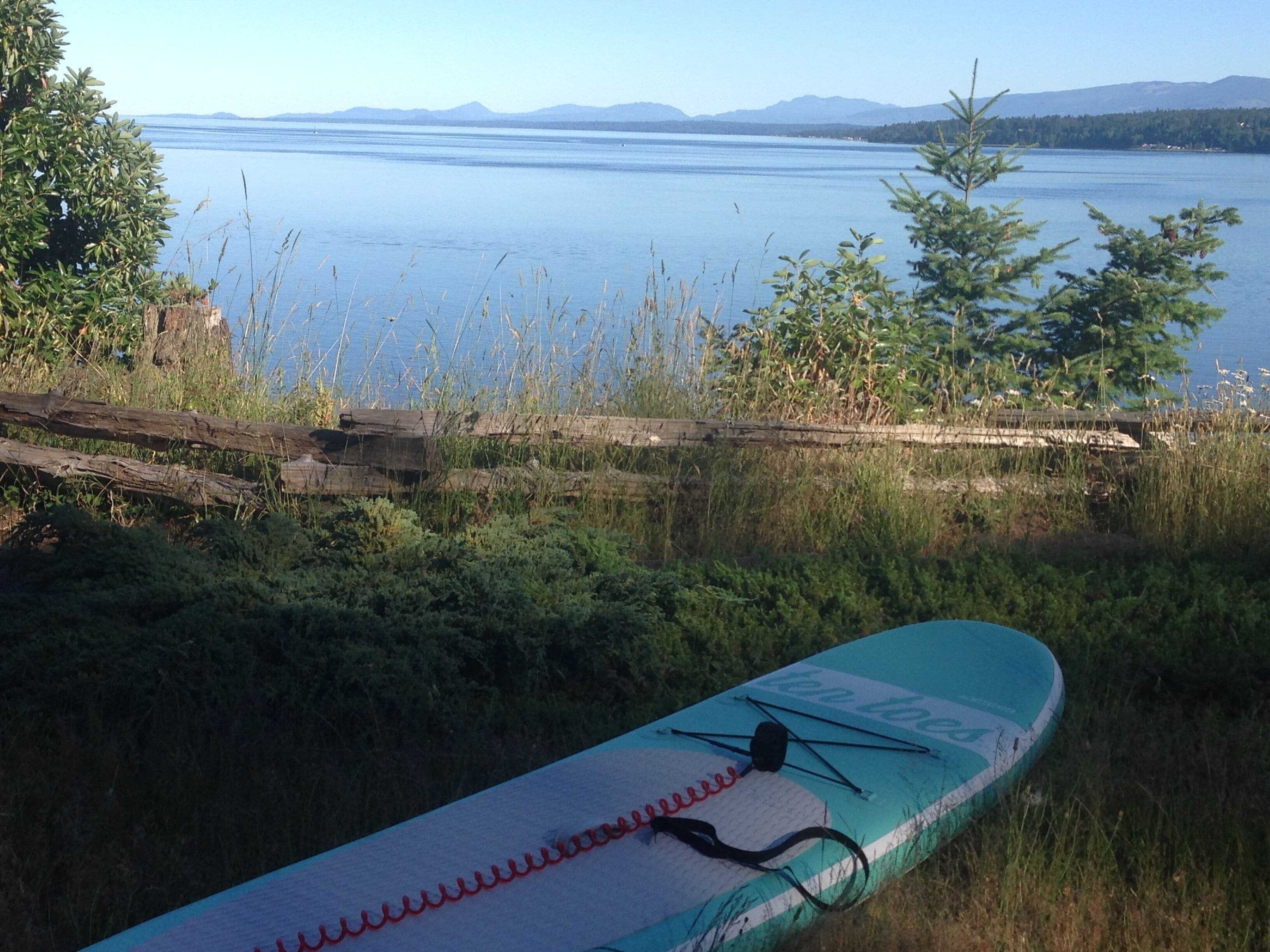 Un kayak est posé sur une rive herbeuse, avec un lac et des montagnes en arrière-plan.