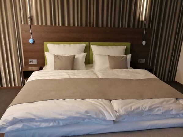 A neatly made bed with white and beige linens, a green headboard, and two bedside tables with lamps. - Steinberger Hof (Dietzenbach)