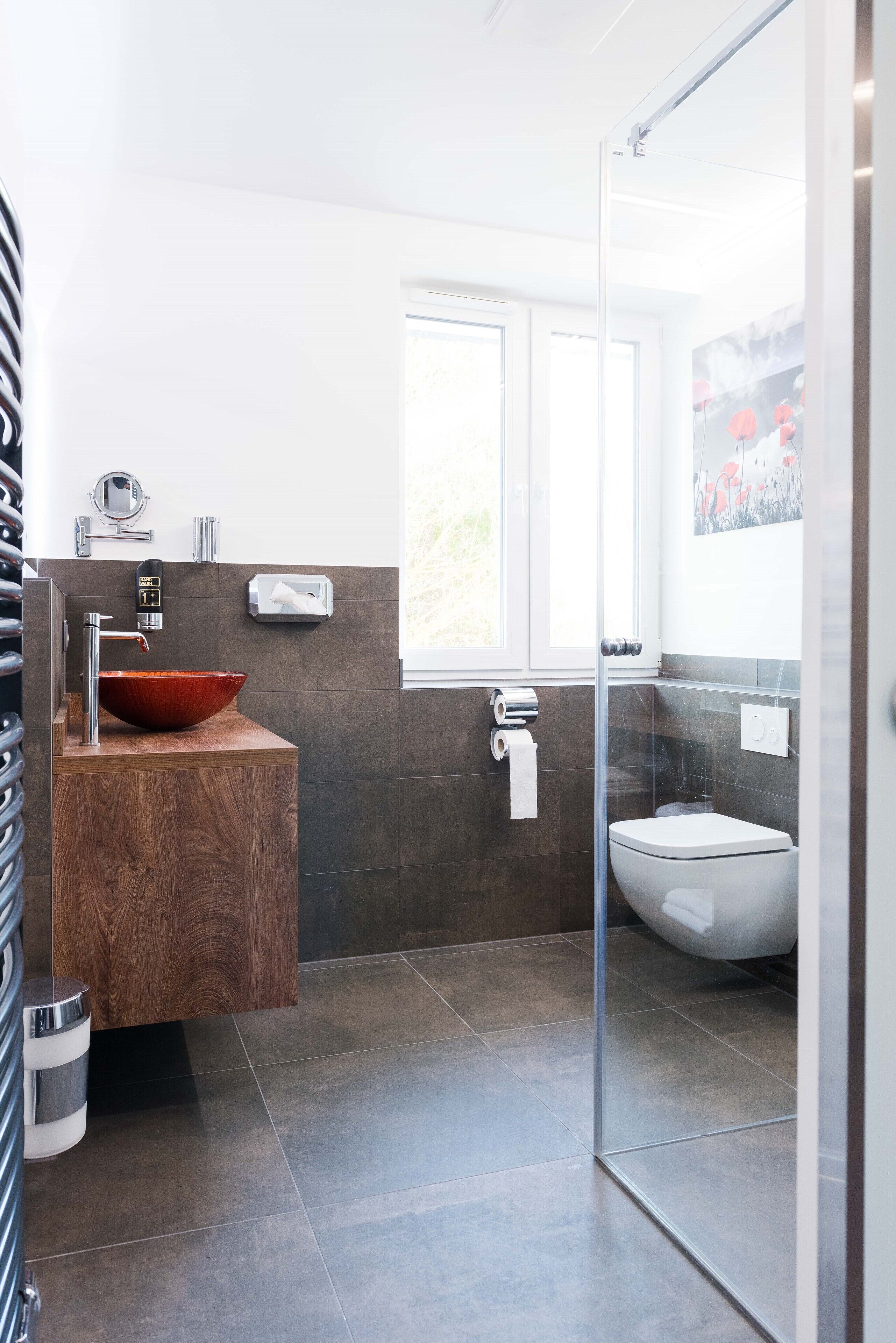 Ein modernes Badezimmer mit einem hölzernen Waschtisch, einem großzügigen Becken, einer Duschkabine aus Glas und einer Toilette.