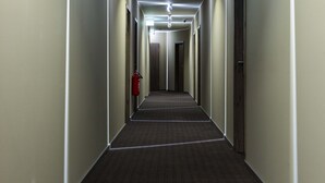 Un long couloir étroit, typique des hôtels, avec un revêtement de sol en moquette, des luminaires encastrés et des portes de part et d’autre.