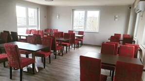 Un espace repas comprenant plusieurs tables et chaises, de grandes fenêtres et un plancher en bois.