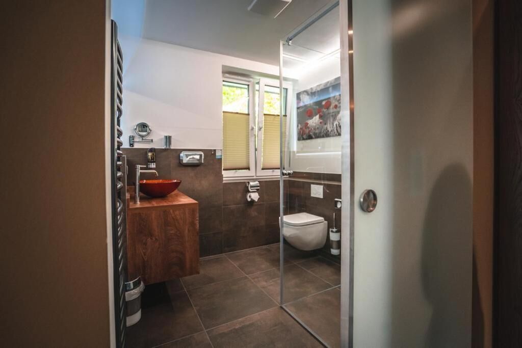 A modern bathroom with a wooden vanity, a glass shower enclosure, and a toilet.