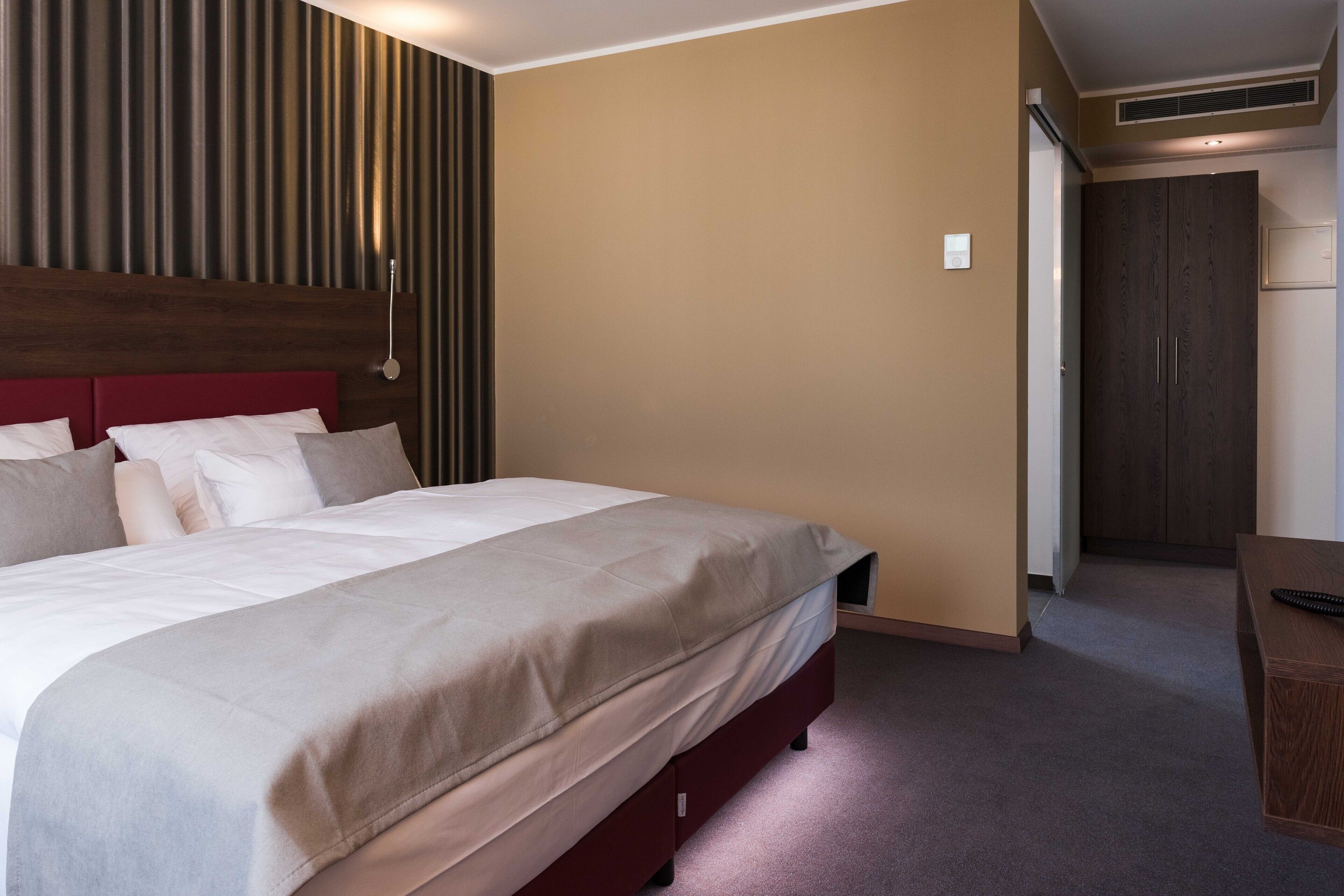 Habitación de hotel con una cama grande, un cabecero de madera, un armario y un escritorio con un control remoto.