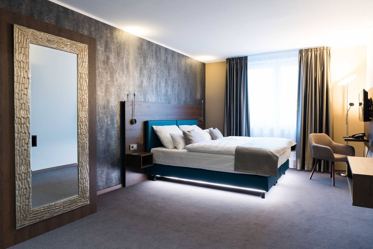 Una habitación de hotel moderna con una cama grande, mesitas de noche, un escritorio y una silla.