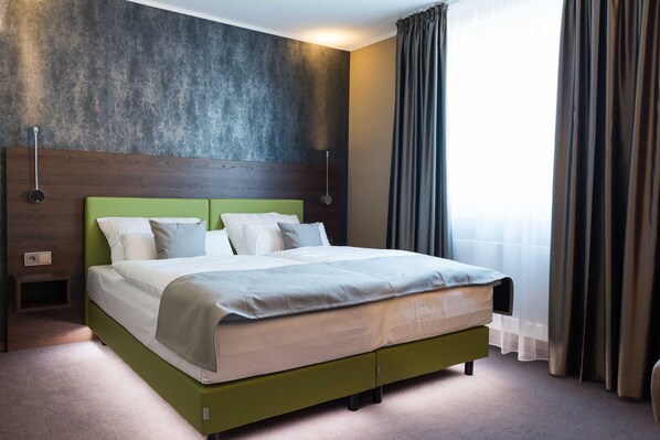 A modern hotel room with a green bed, a wooden headboard, a large window with curtains, and a textured wall. - Steinberger Hof (Dietzenbach)