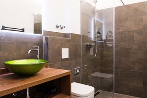 Un baño moderno con un lavabo de vidrio verde, cabina de ducha e inodoro.