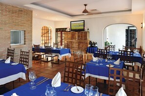 A restaurant with blue tablecloths, wooden chairs, and a television on the wall.