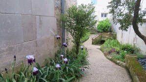 A narrow gravel path flanked by lush greenery and flowering plants, leading to a stone bridge and a building with a white facade. - 3- Star small town cutie on the Charente River (Bourg-Charente)