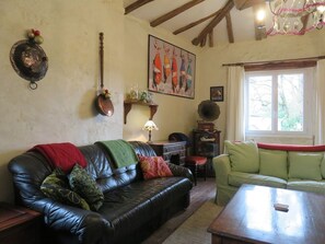 Ein gemütliches Wohnzimmer mit Ledersofa, einem grünen Sessel und einem Holztisch. An der Wand hängt ein Kamin mit Sims und einem gerahmten Bild.