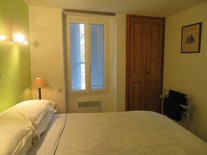 Ein Schlafzimmer mit Bett, Fenster, Tür, Heizkörper und Lampe.