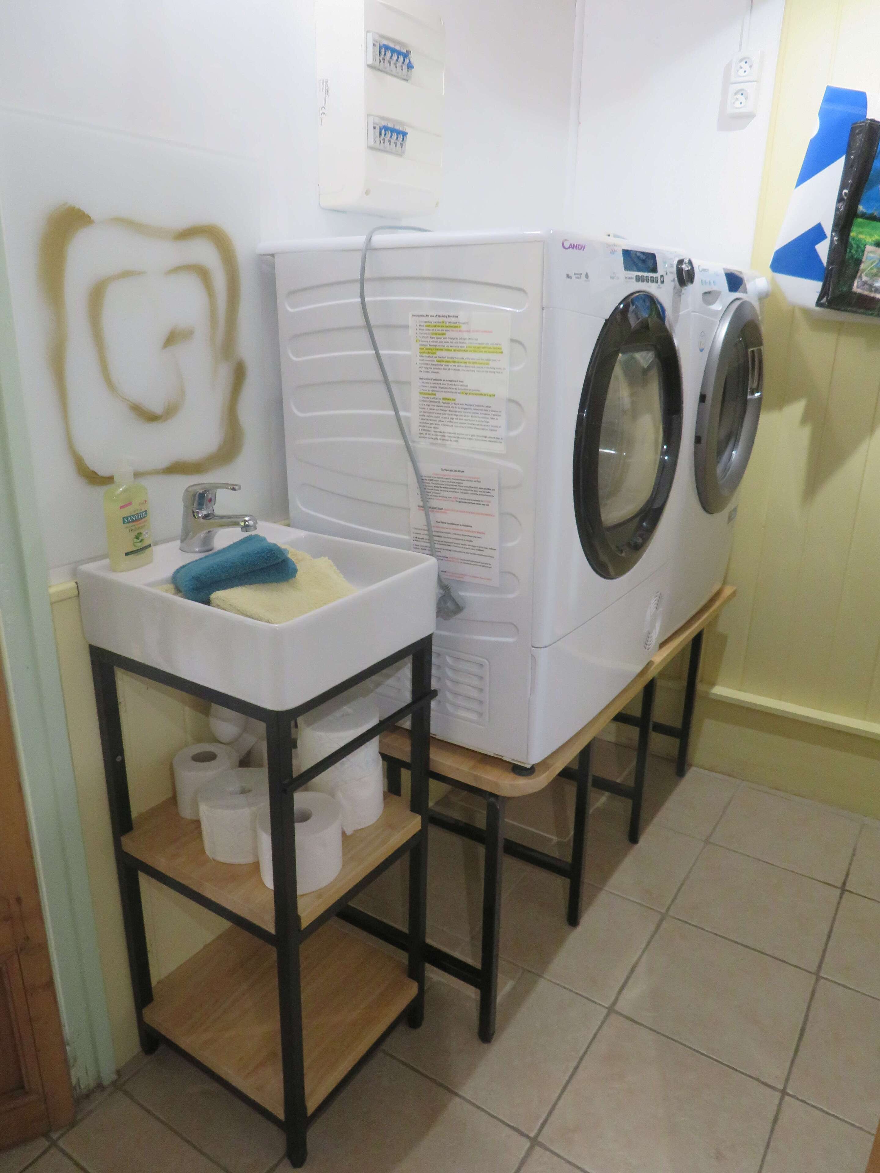 Ein Waschbereich mit Waschmaschine, einem Waschbecken mit blauem Handtuch und einer Ablage mit Toilettenpapier.