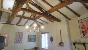 A rustic room with exposed wooden beams, a chandelier, a television, a painting, and a window with curtains. - 3- Star small town cutie on the Charente River (Bourg-Charente)