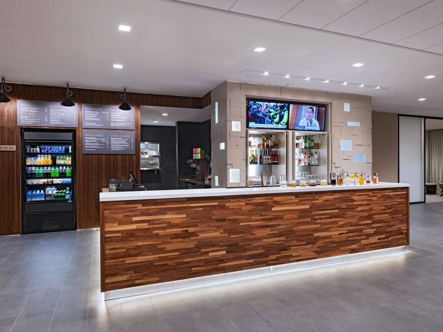 A modern bar area with a wooden counter, a beverage dispenser, and a television screen.