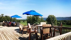 Una terraza de madera con mobiliario exterior y sombrillas, con vistas a un paisaje pintoresco.