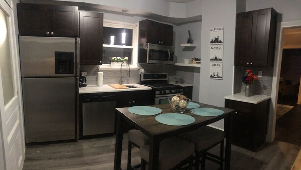A compact kitchen with dark wood cabinets, stainless steel appliances, and a dining area with a wooden table and chairs. - Cozy, Comfortable and Convenient apartment. Close to everything! (Oak Park)