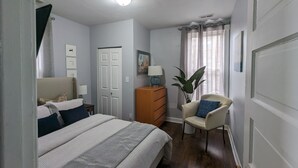 A bedroom with a bed, a dresser, a chair, a plant, and a door. - Cozy, Comfortable and Convenient apartment. Close to everything! (Oak Park)
