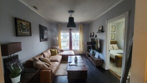 A living room with a sofa, coffee table, TV, and a large window with curtains. - Cozy, Comfortable and Convenient apartment. Close to everything! (Oak Park)