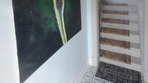 A hallway with a large abstract painting, a patterned floor, and a staircase with decorative railings. - Cozy, Comfortable and Convenient apartment. Close to everything! (Oak Park)