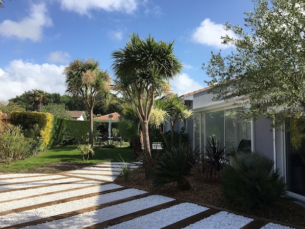 A well-maintained garden with a wooden pathway leading to a house with a glass door.