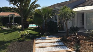 Ein Haus mit Swimmingpool, umgeben von Palmen und einem Garten mit Kiesweg.