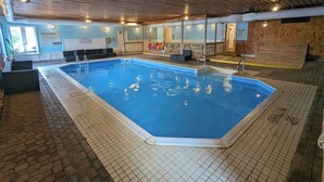 An indoor swimming pool with a tiled floor, wooden ceiling, and a poolside area with seating and a lifeguard station. - Great Blue Resorts - McCreary's Beach (Drummond-North Elmsley)