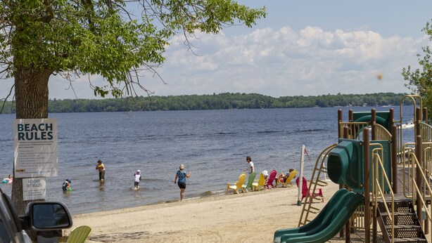 A beach with a playground, including slides and swings, and a sign indicating beach rules. - Great Blue Resorts - McCreary's Beach (Drummond-North Elmsley)