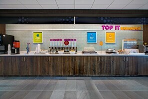 Una barra de desayuno con un letrero que dice "TOP IT BREAKFAST" y diversos alimentos exhibidos.