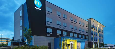 A modern hotel with a prominent 'tru by Hilton' sign, multiple floors, and a well-lit entrance.