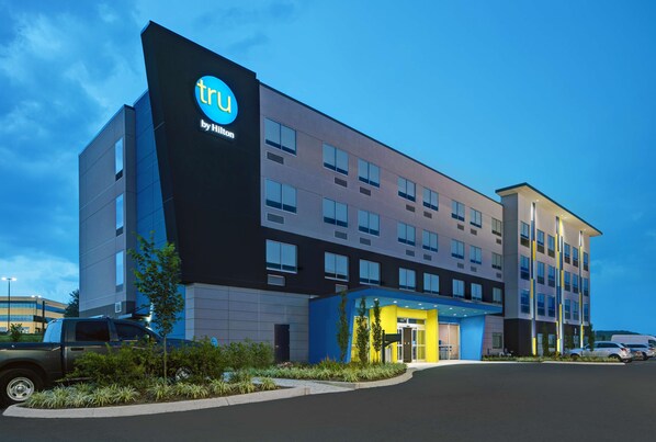 Un hotel moderno con un llamativo letrero de 'tru by Hilton', varios pisos y una entrada bien iluminada.