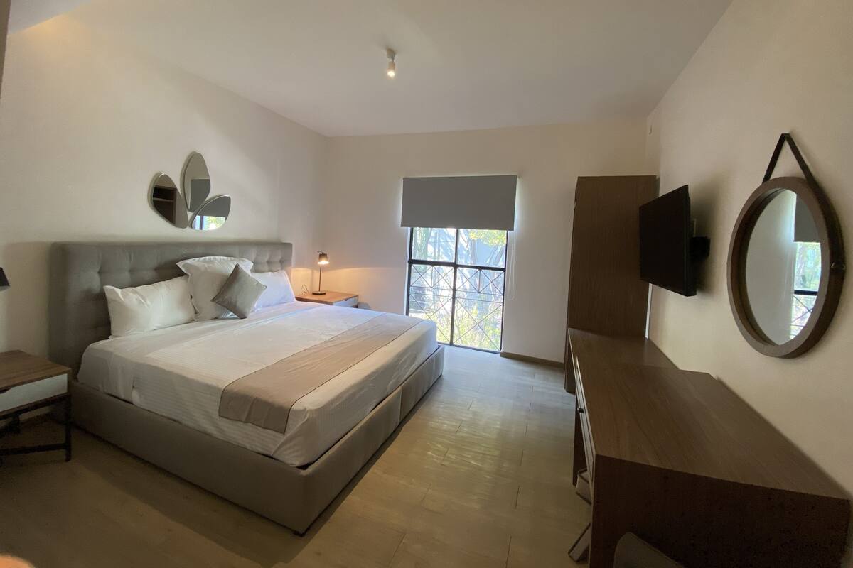 A modern bedroom with a large bed, bedside tables, a TV, and a window with a view.