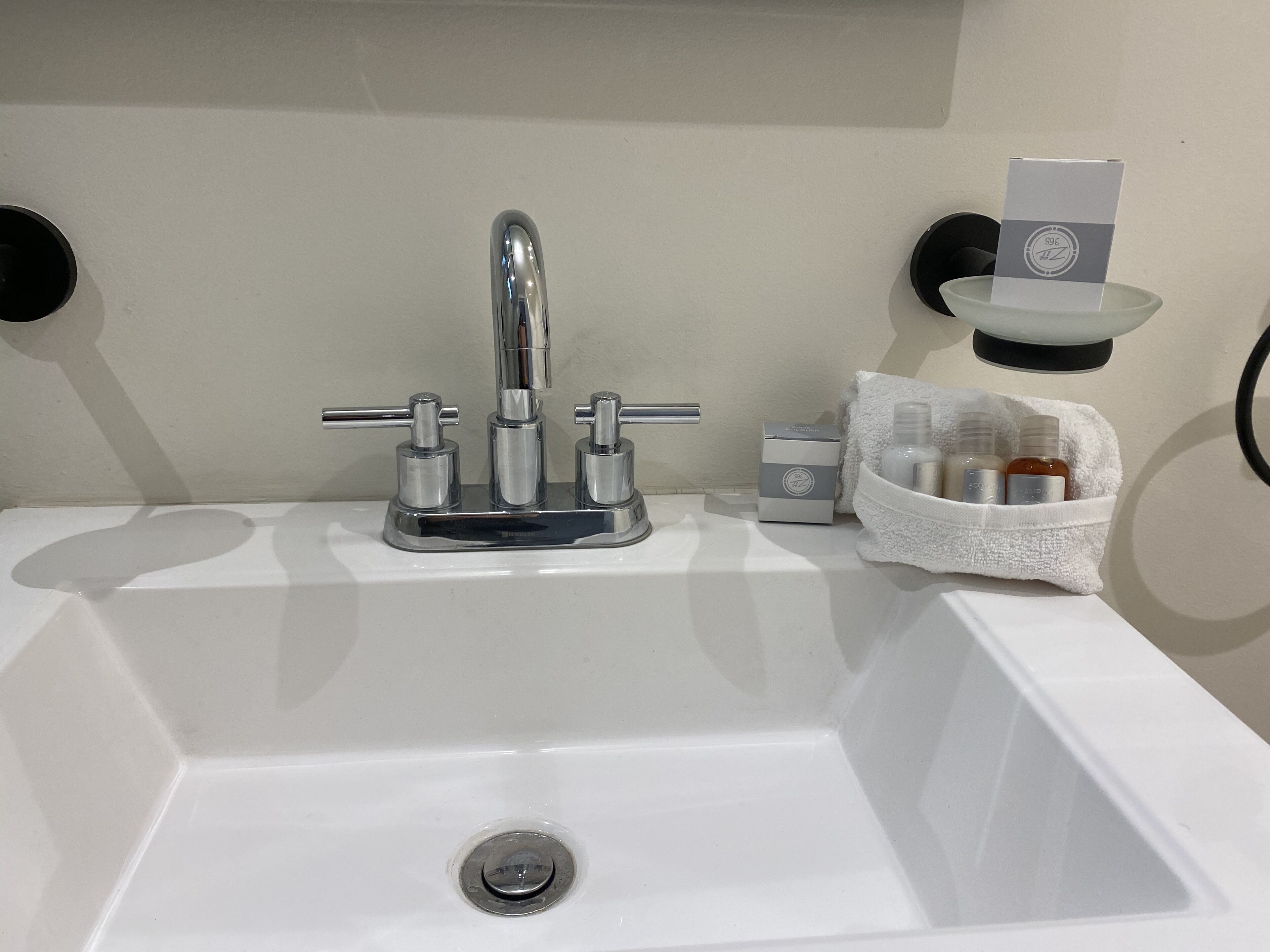 A white bathroom sink with a chrome faucet, a soap dispenser, and a small bottle of shampoo.